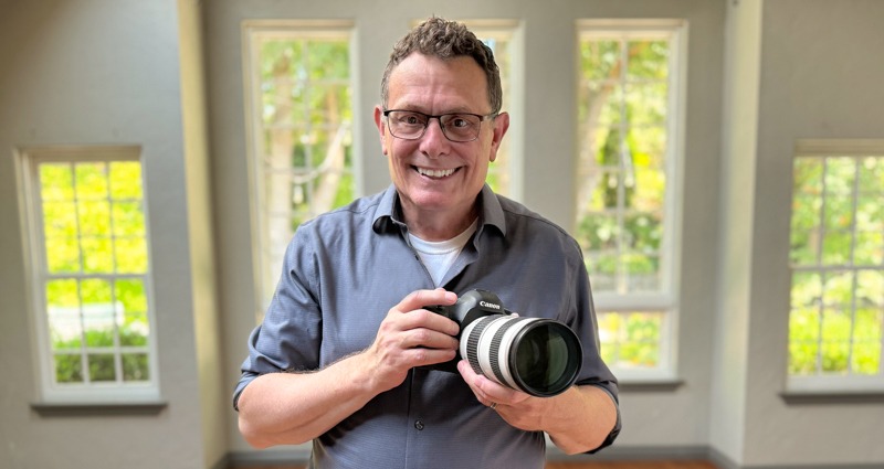 Terry Cyr holding a camera with a telephoto lens beside a studio window